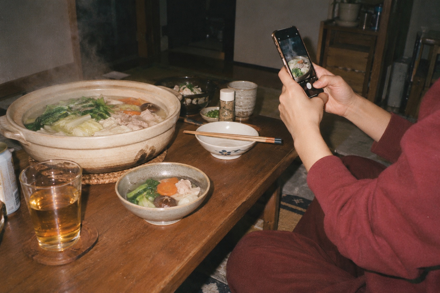 湯気の立つ鍋料理をスマートフォンで撮影する食卓
